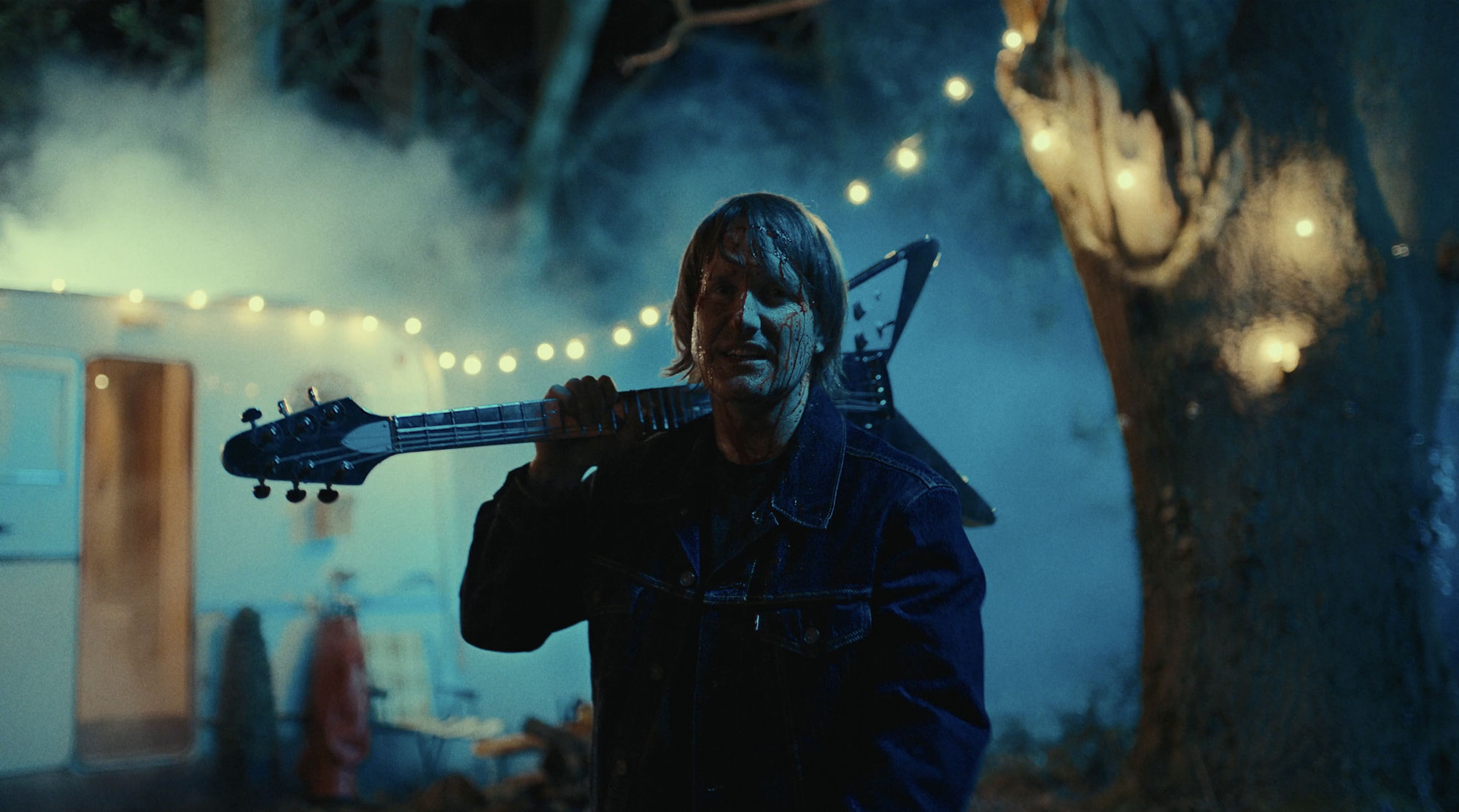 Tim Wheeler in the dark with a Gibson Flying V guitar behind his head and blood on his face
